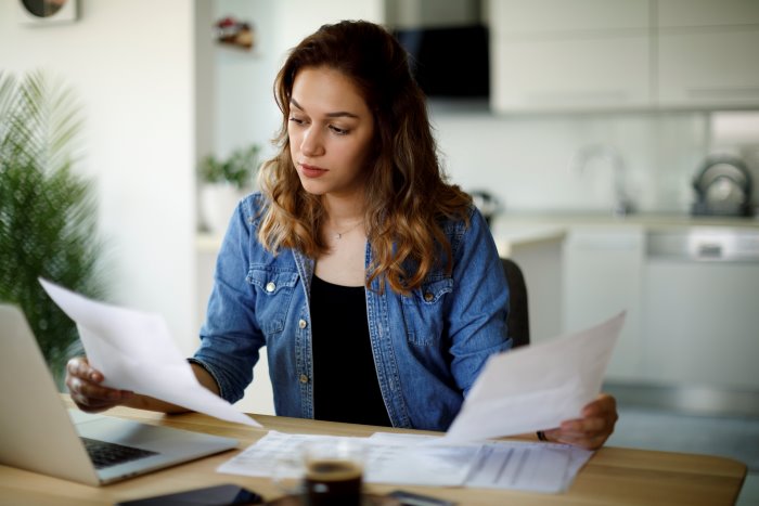 Woman looking through tax documents in front of a laptop. 