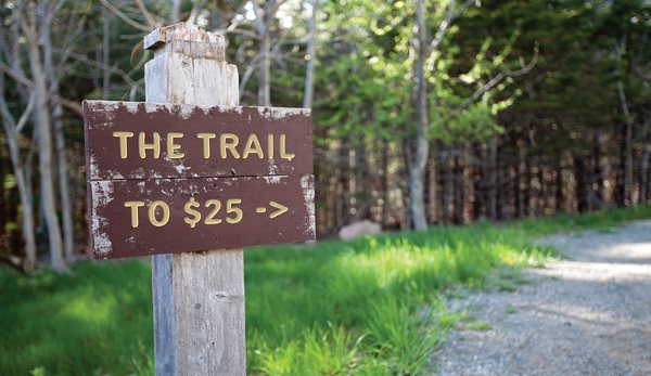 Trail sign stating, "The trail to $25" with an arrow point down the trail. 