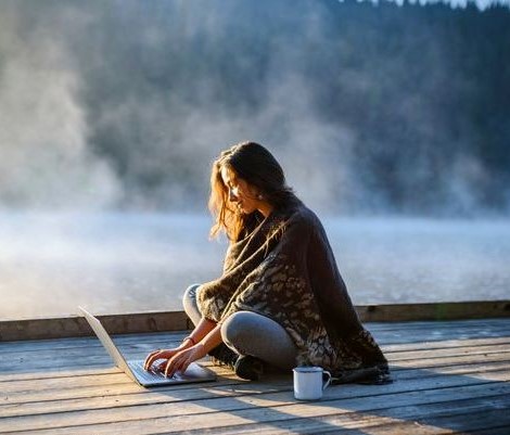 Woman sitting on a dock with her laptop and coffee